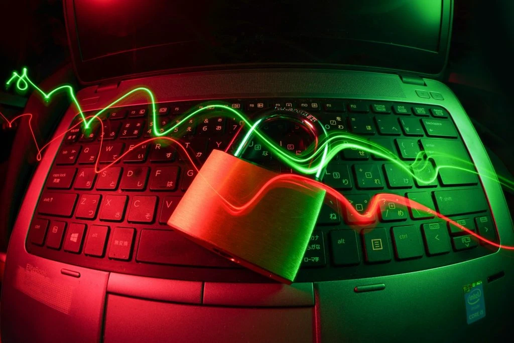 Cybersecurity concept with a physical padlock on a laptop keyboard and neon green and red light streaks.