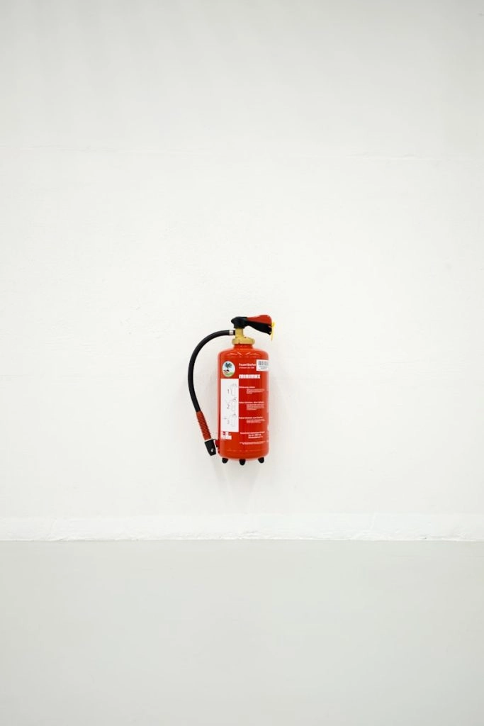 A red fire extinguisher is mounted centered on a plain white wall above a lower, slightly darker horizontal section