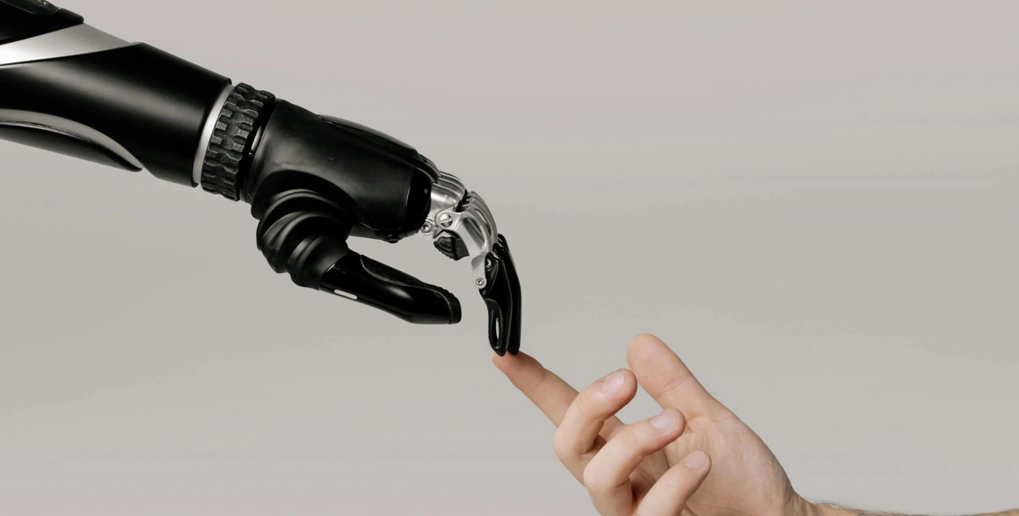 A close-up shot of a sleek, black robotic hand and a human hand gently touching index fingers against a plain, light grey background