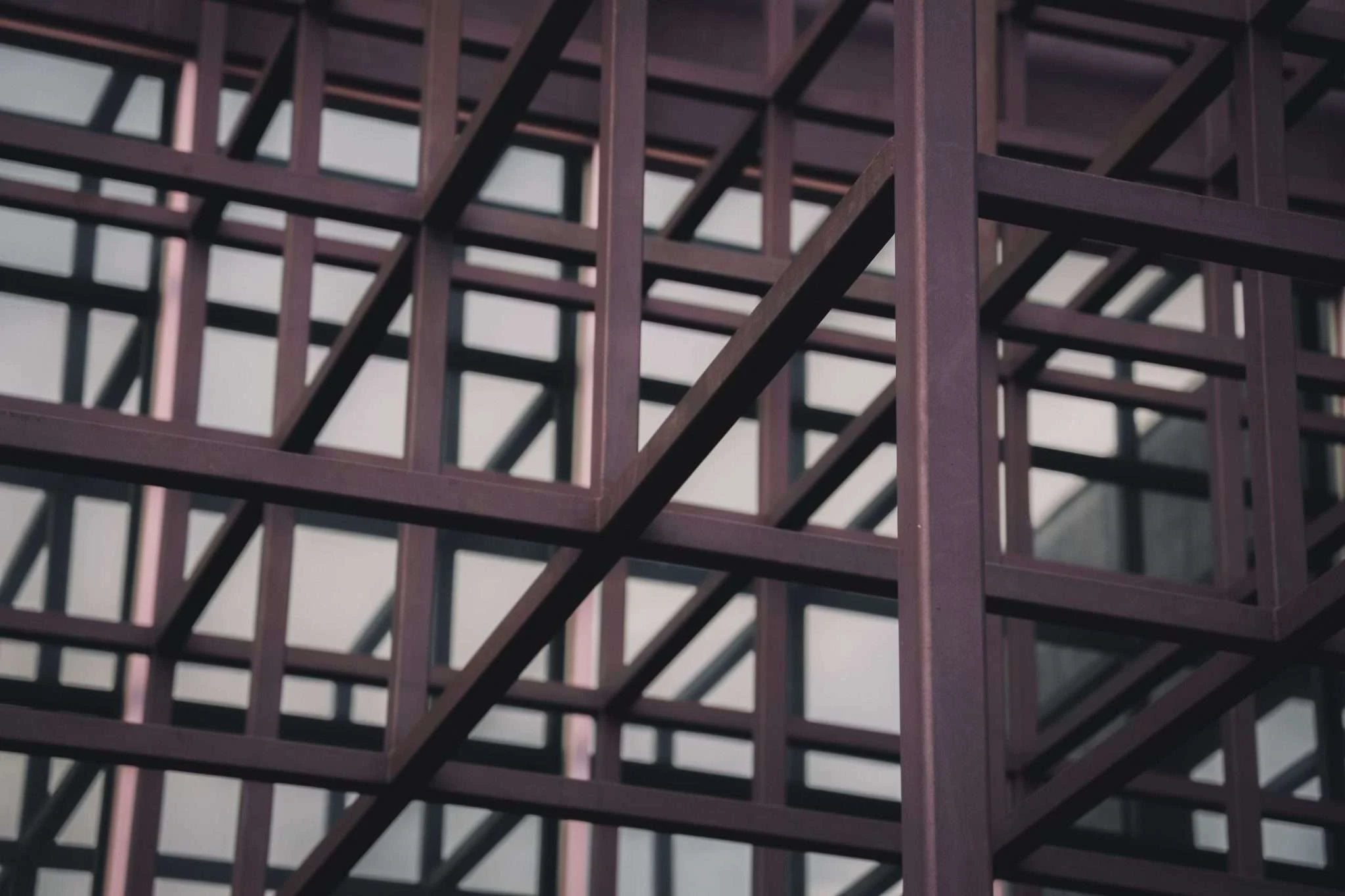 A close-up shot of a dark-colored geometric metal structure forming a grid pattern, with a blurred building visible in the background.