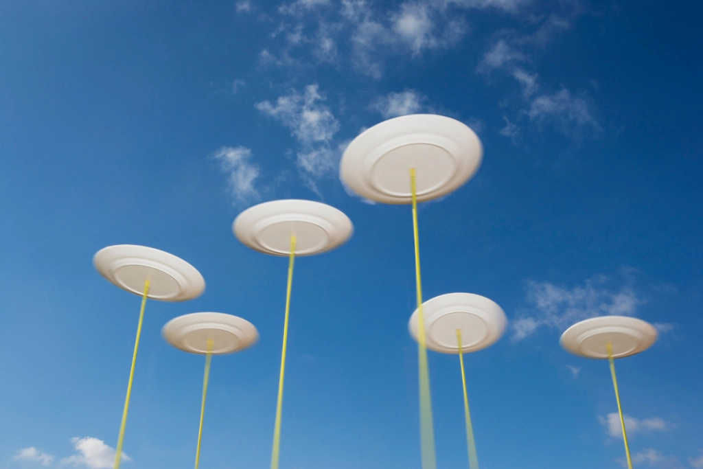 Six white ceramic plates spinning on top of tall, thin yellow poles against a clear blue sky with light, wispy clouds.