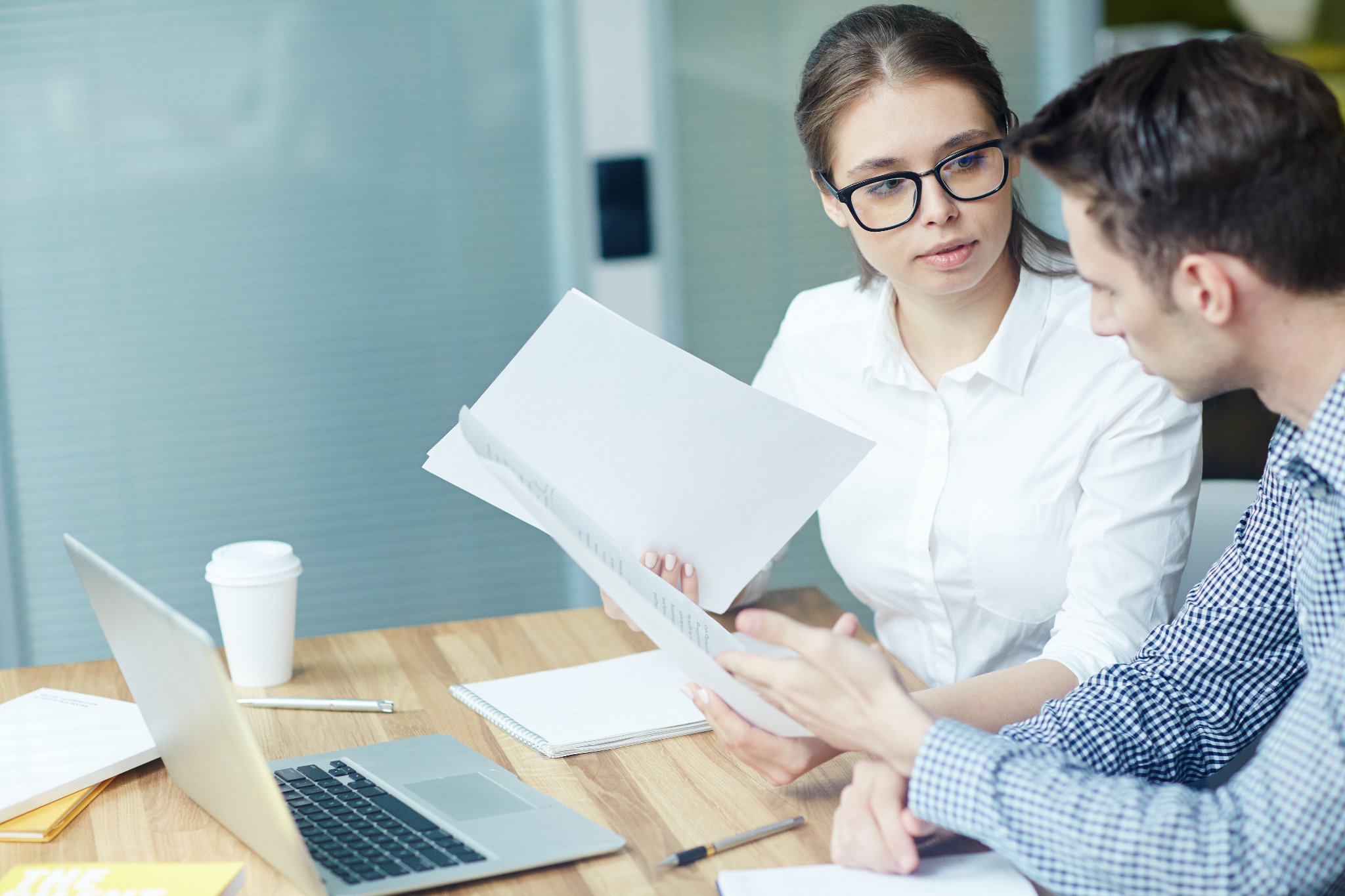 Two colleagues reviewing printed documents together at a desk.