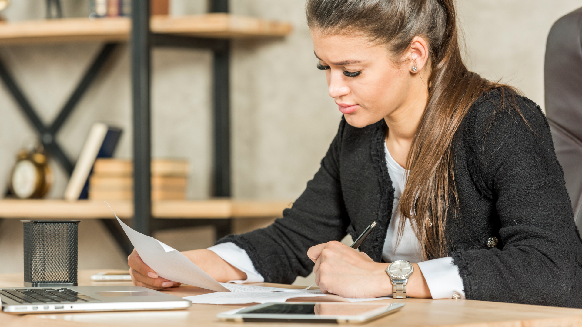 Professional reviewing documents at a desk with a laptop and phone nearby.
