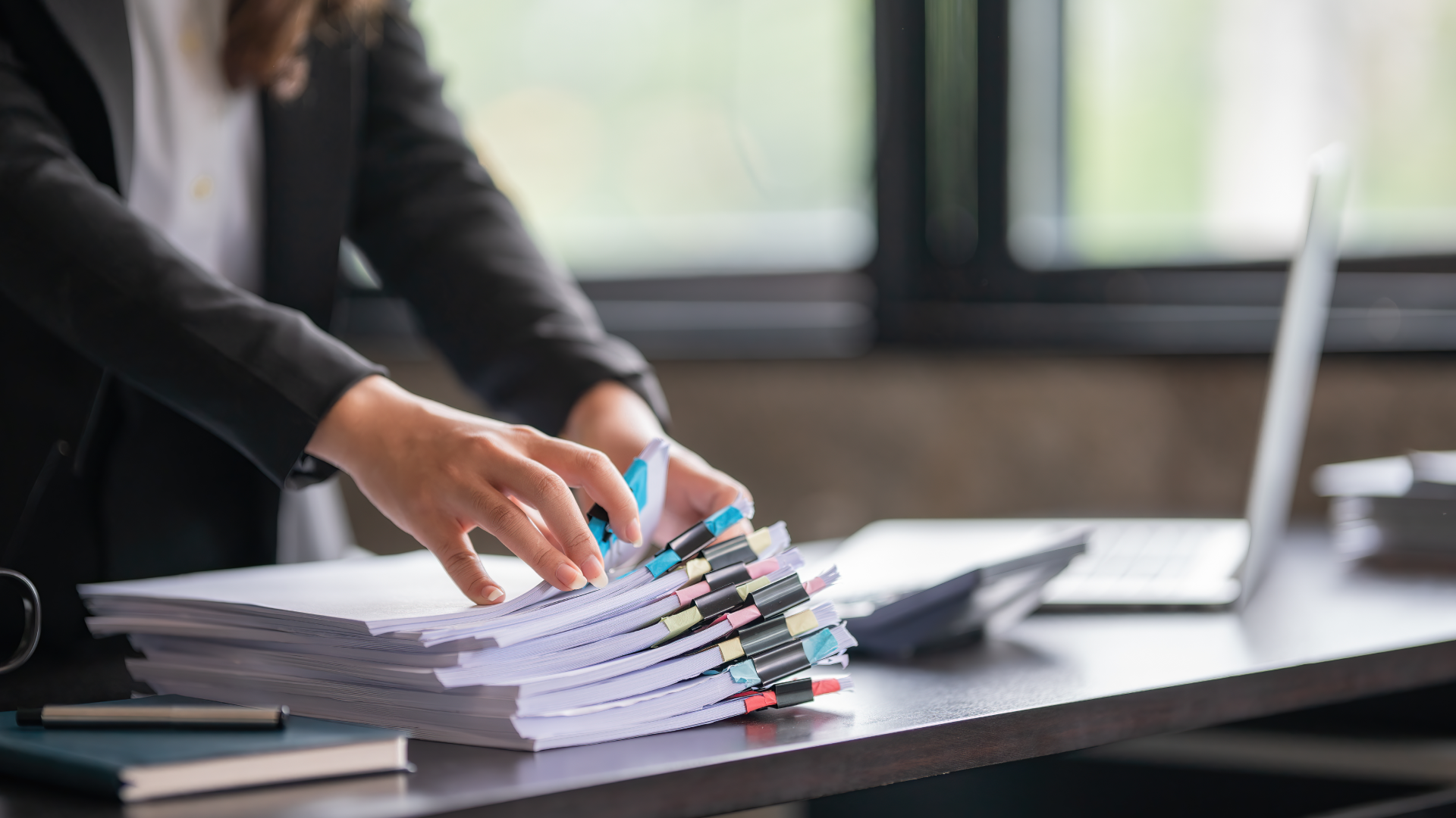 Close-up of a professional sorting through a large stack of tabbed documents on a desk.