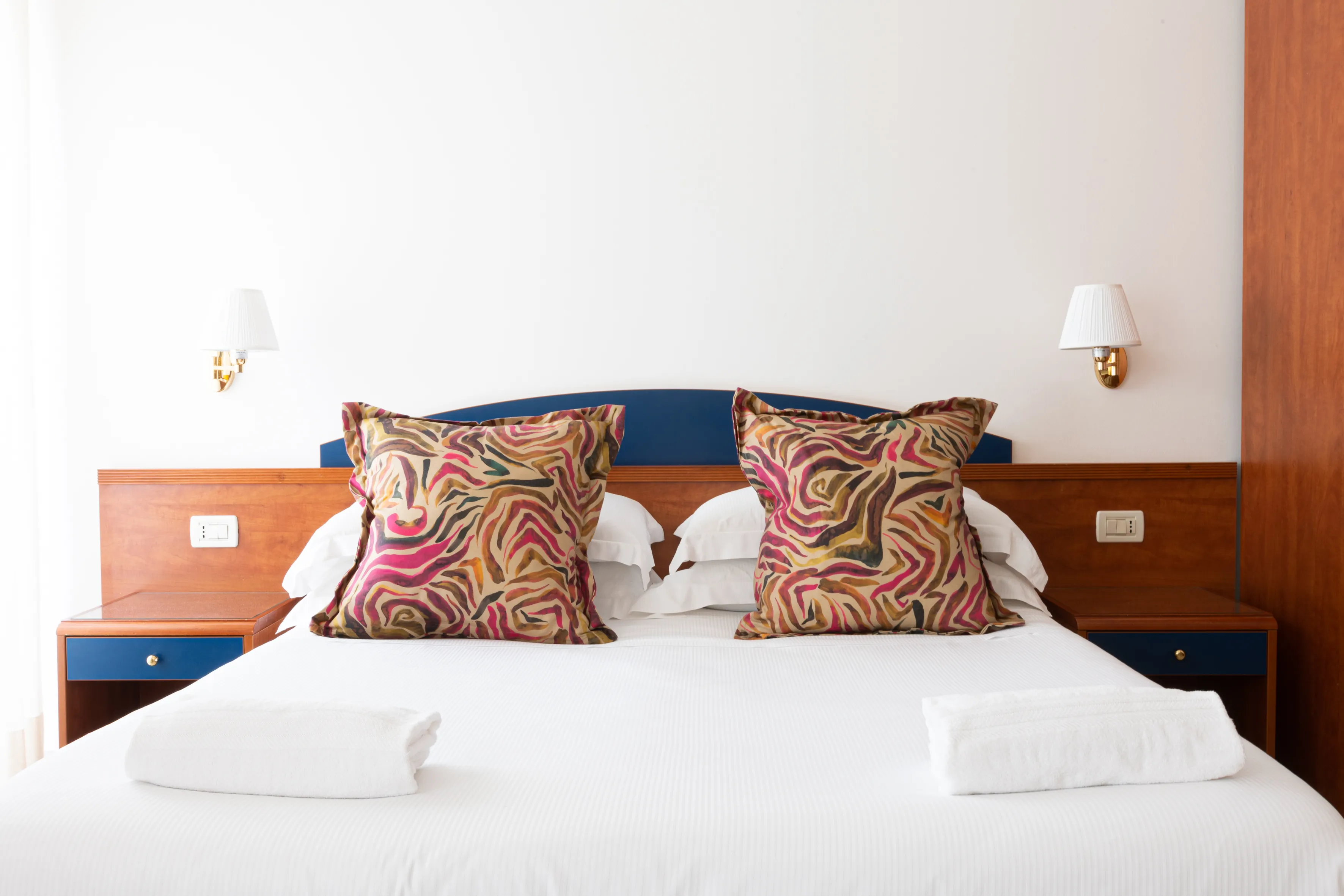 Bagno con lavabo bianco, specchio, asciugamani arrotolati bianchi e blu, dispenser per sapone e piastrelle gialle e beige.