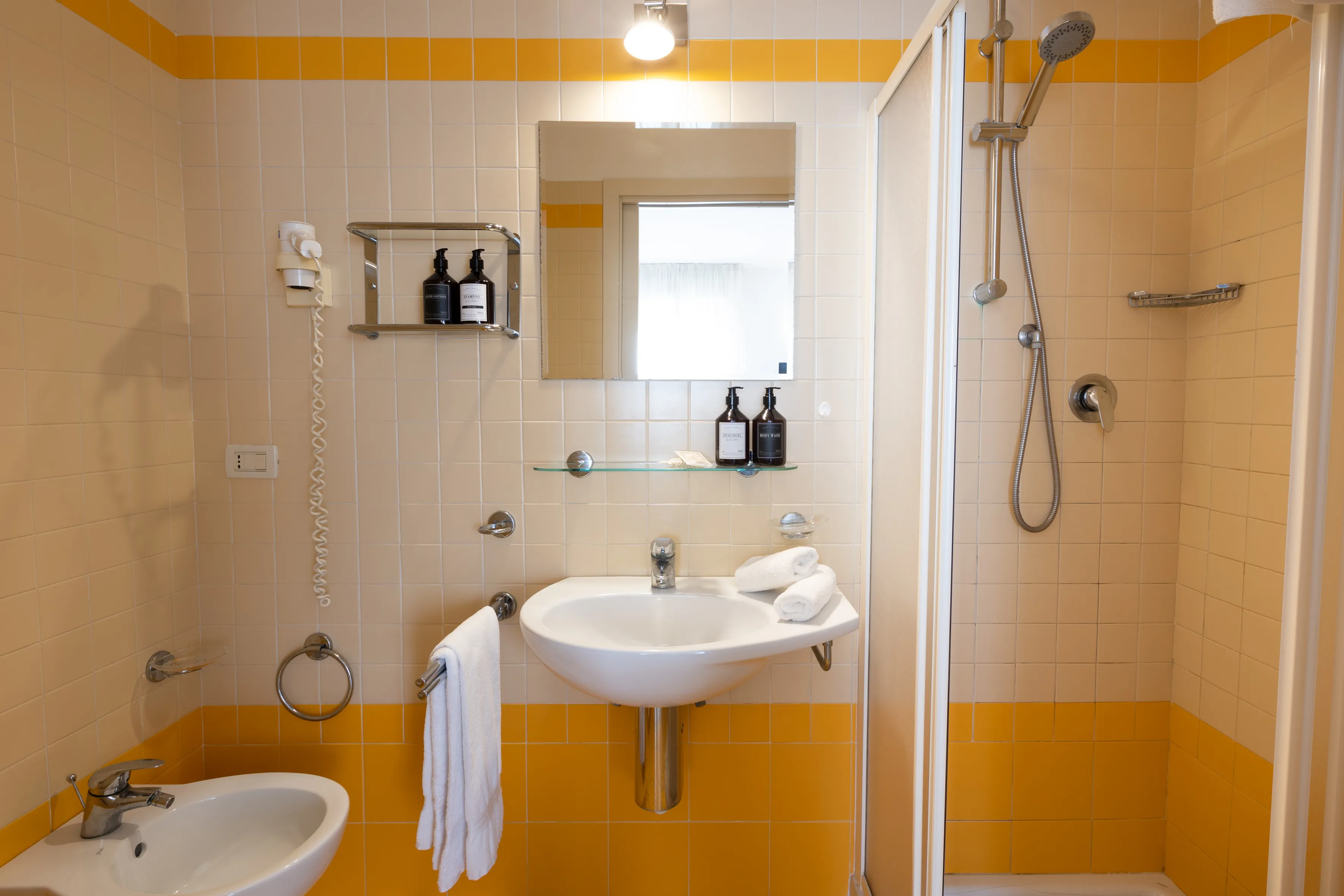 Interno luminoso con tavolo bianco apparecchiato per due, sedie gialle e letto singolo con copriletto bianco.