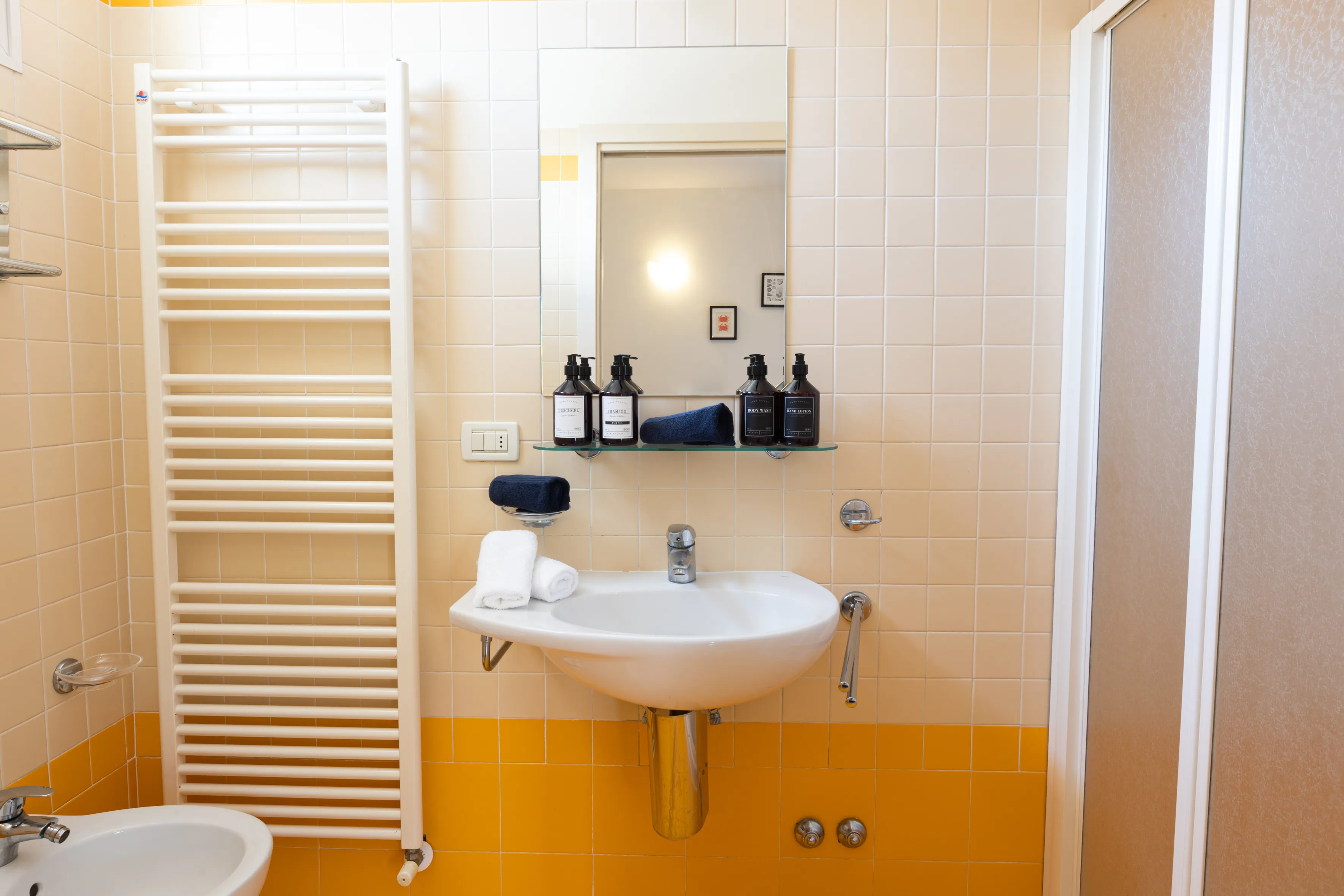 Bagno con doccia, wc, bidet, lavabo con asciugamani arrotolati e prodotti da bagno su una mensola.