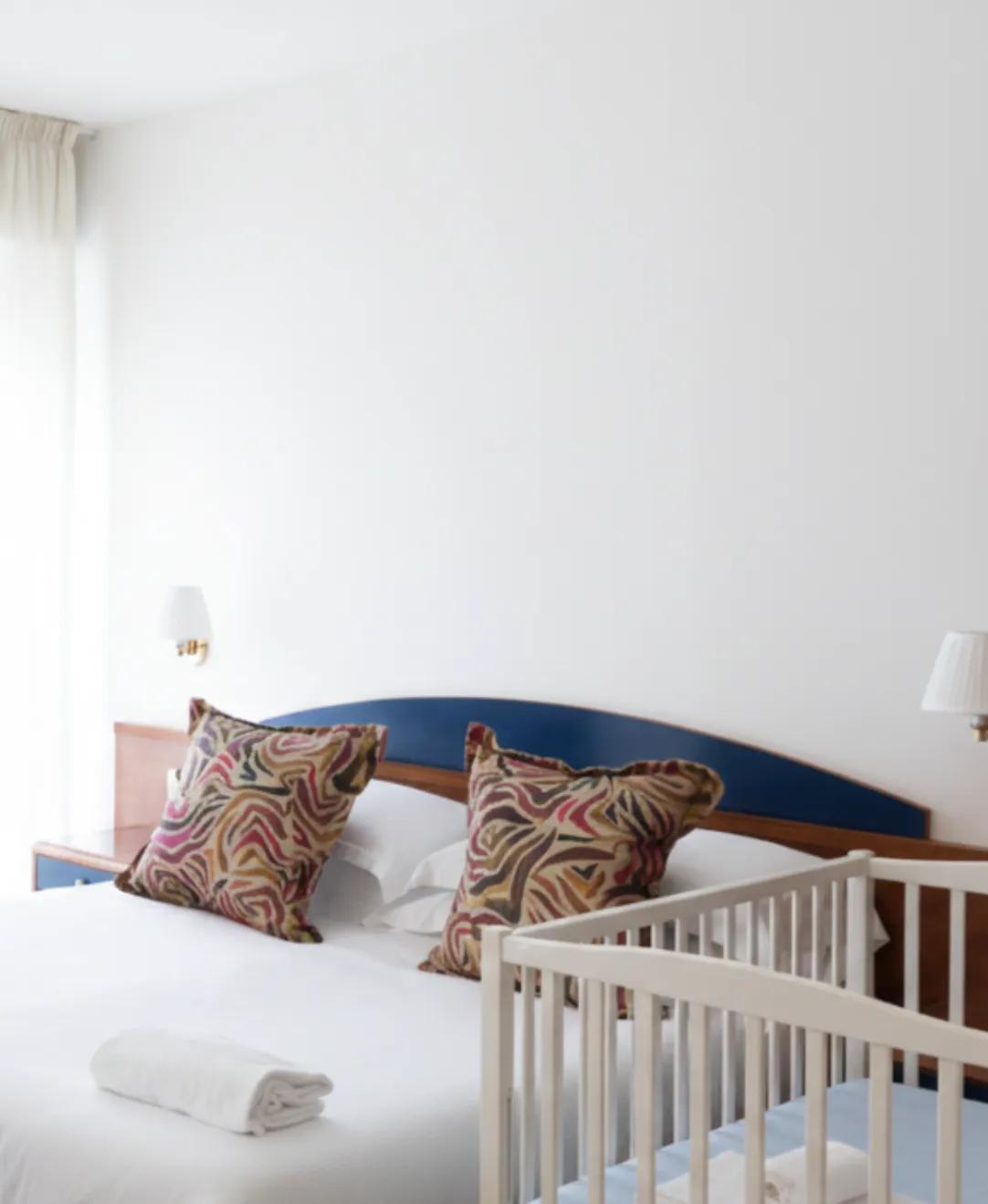 Camera da letto con letto matrimoniale con cuscini decorativi e culla bianca in primo piano.