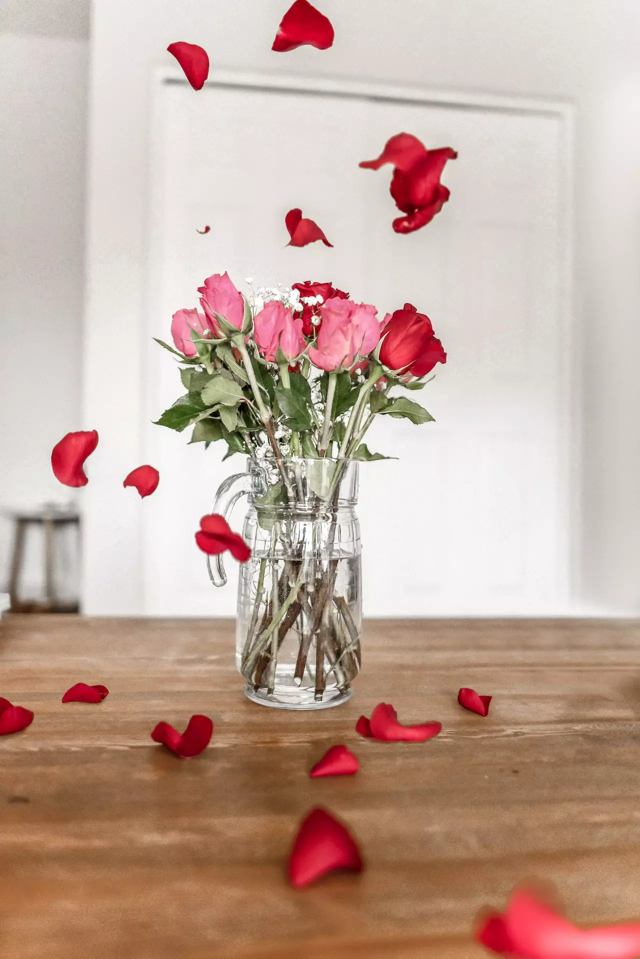 A vase of pink and red roses with petals spread around