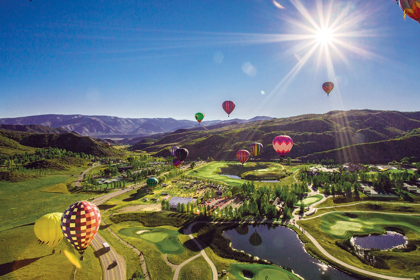 hot air balloons floating up over sunny green Aspen valley