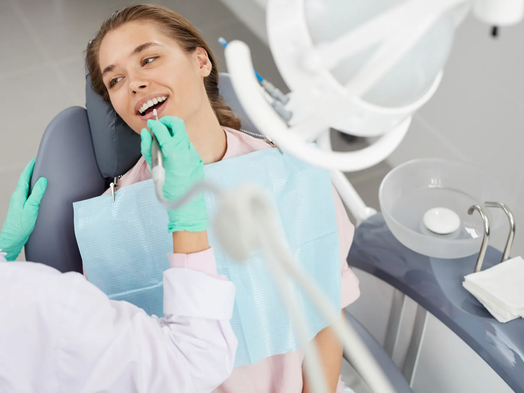 A woman sitting in a dentist chair with a toothbrush in her mouth.