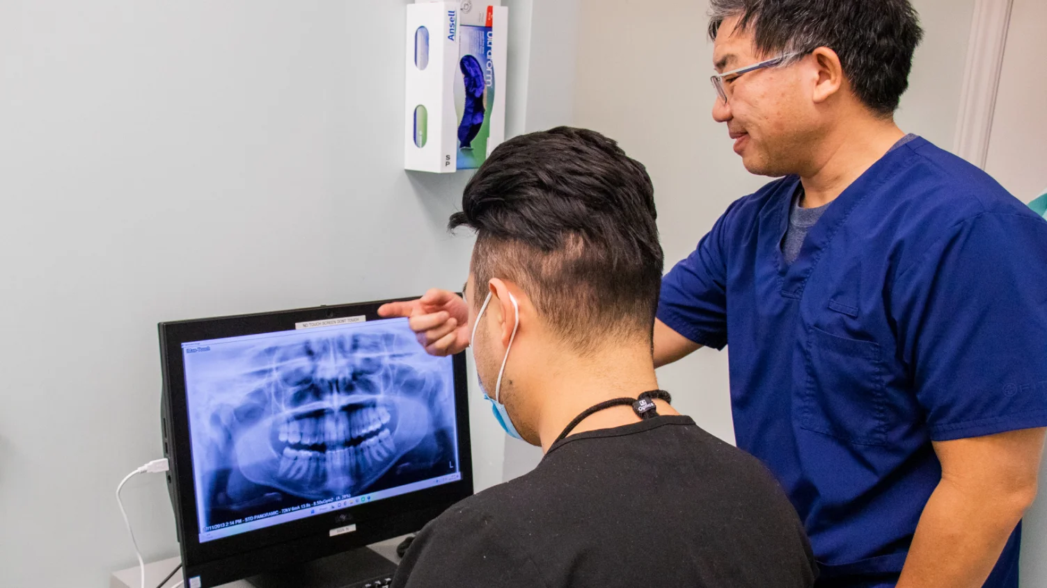 A man in scrubs is looking at a computer screen.