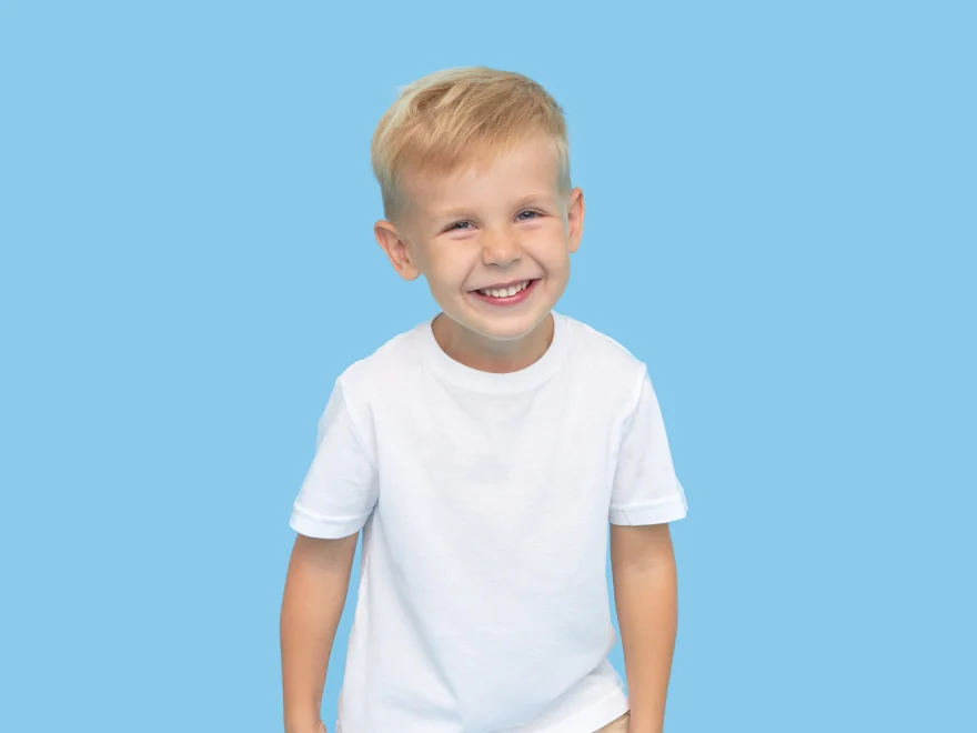A young boy in a white t - shirt smiles at the camera.