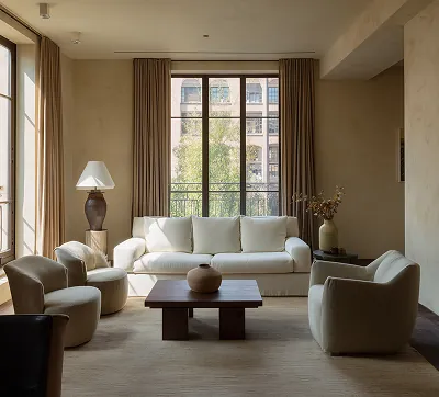 A modern living room featuring two large windows, minimalist design, and warm wooden floors and furniture, highlighting a seamless blend of comfort and architectural elegance.