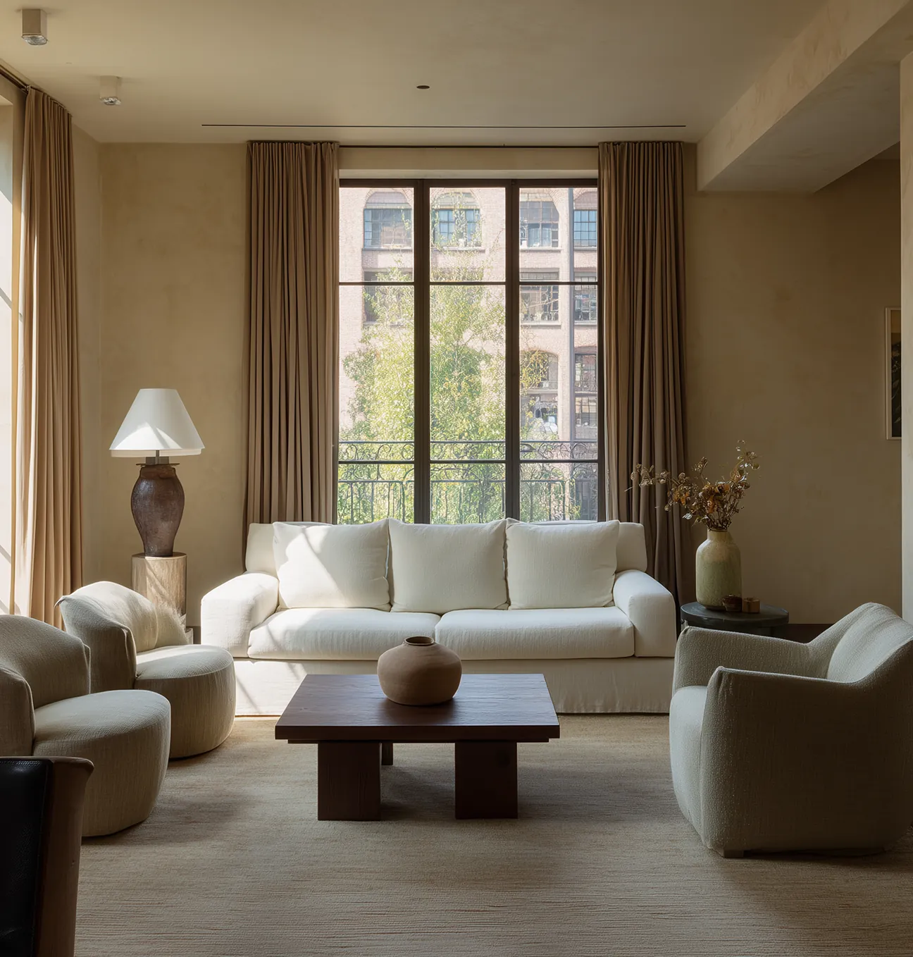 A modern living room featuring two large windows, minimalist design, and warm wooden floors and furniture, highlighting a seamless blend of comfort and architectural elegance.