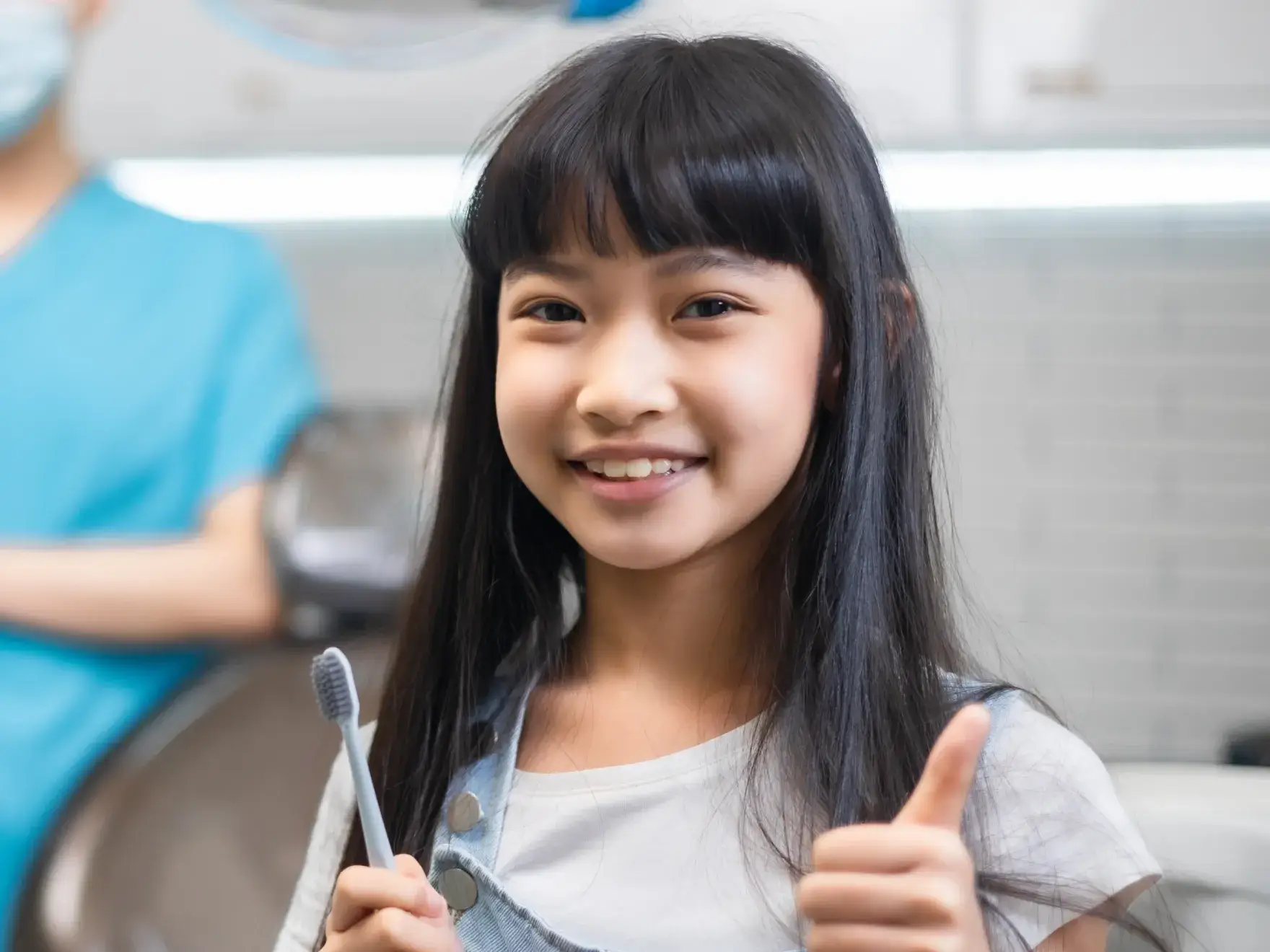 Young girl smiling, holding a toothbrush and giving a thumbs up.