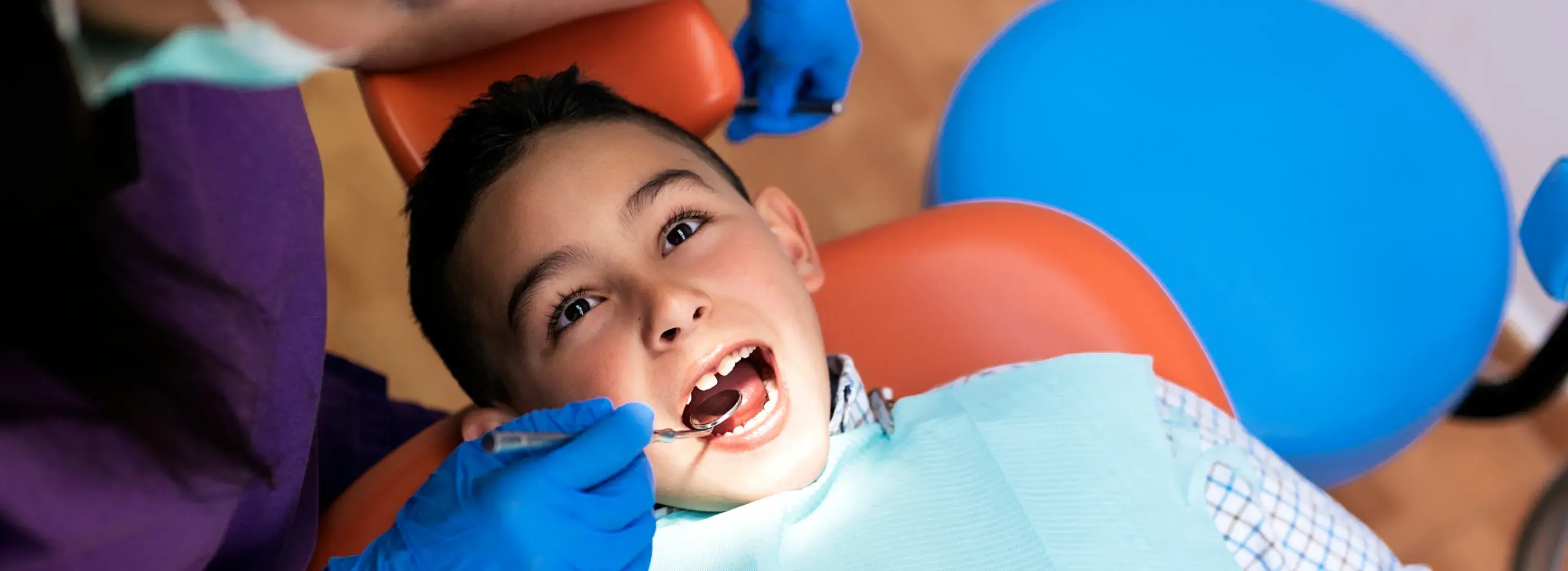 A dentist examines a boy's teeth while he sits in a dental chair.