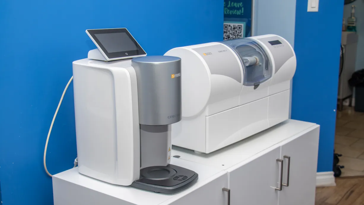 Two dental machines are on a white cabinet against a blue wall, ready for use.