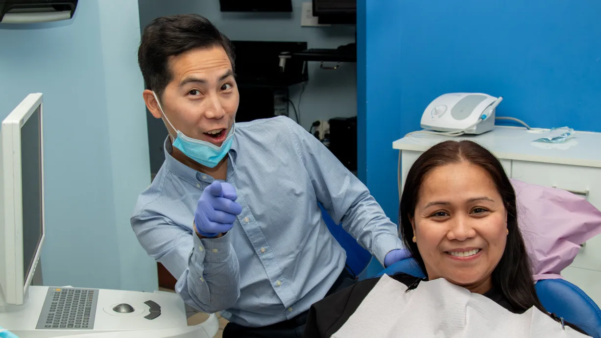 A dentist and a smiling patient pose together in a dental office.