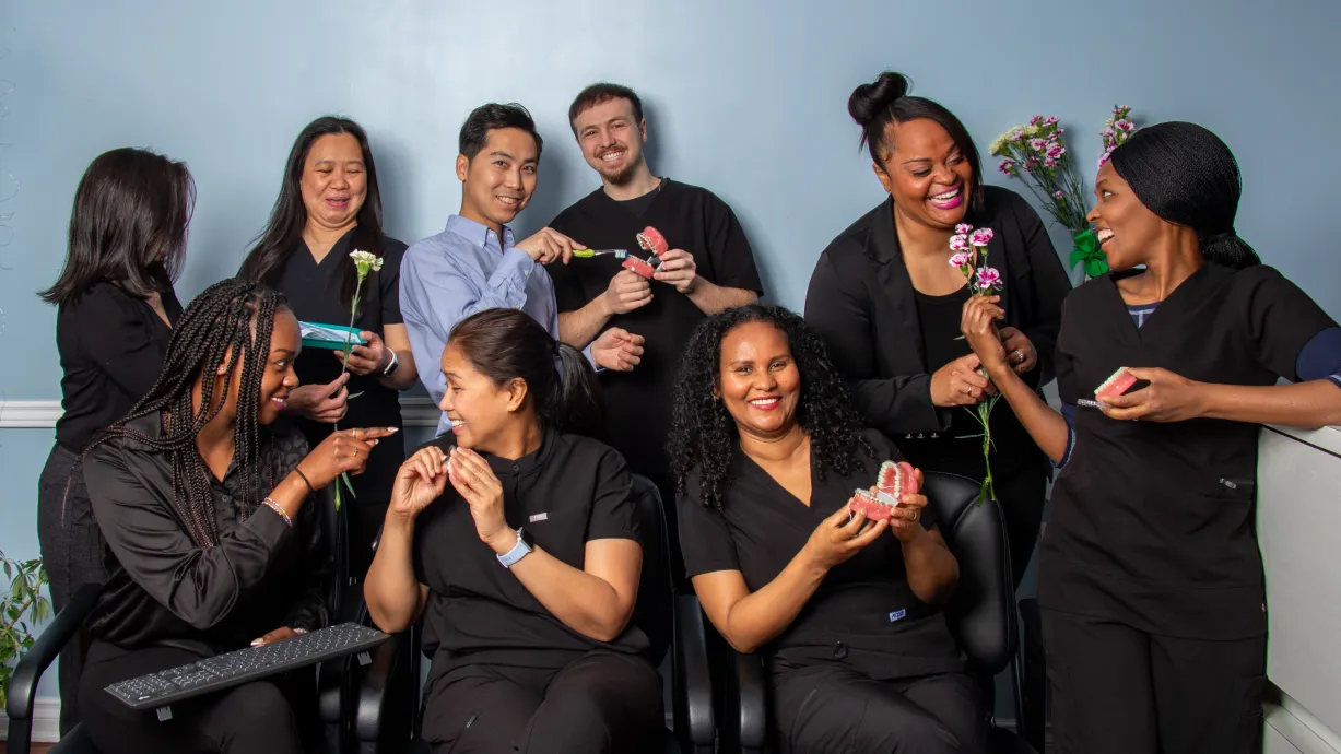 A woman smiles while examining a dental model with a dental instrument, wearing a black shirt.