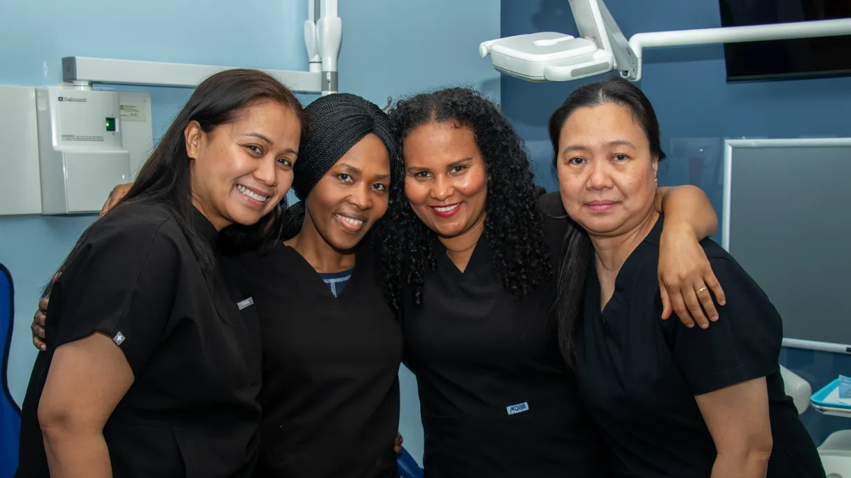 A dentist and patient both give thumbs up while smiling in a dental office.