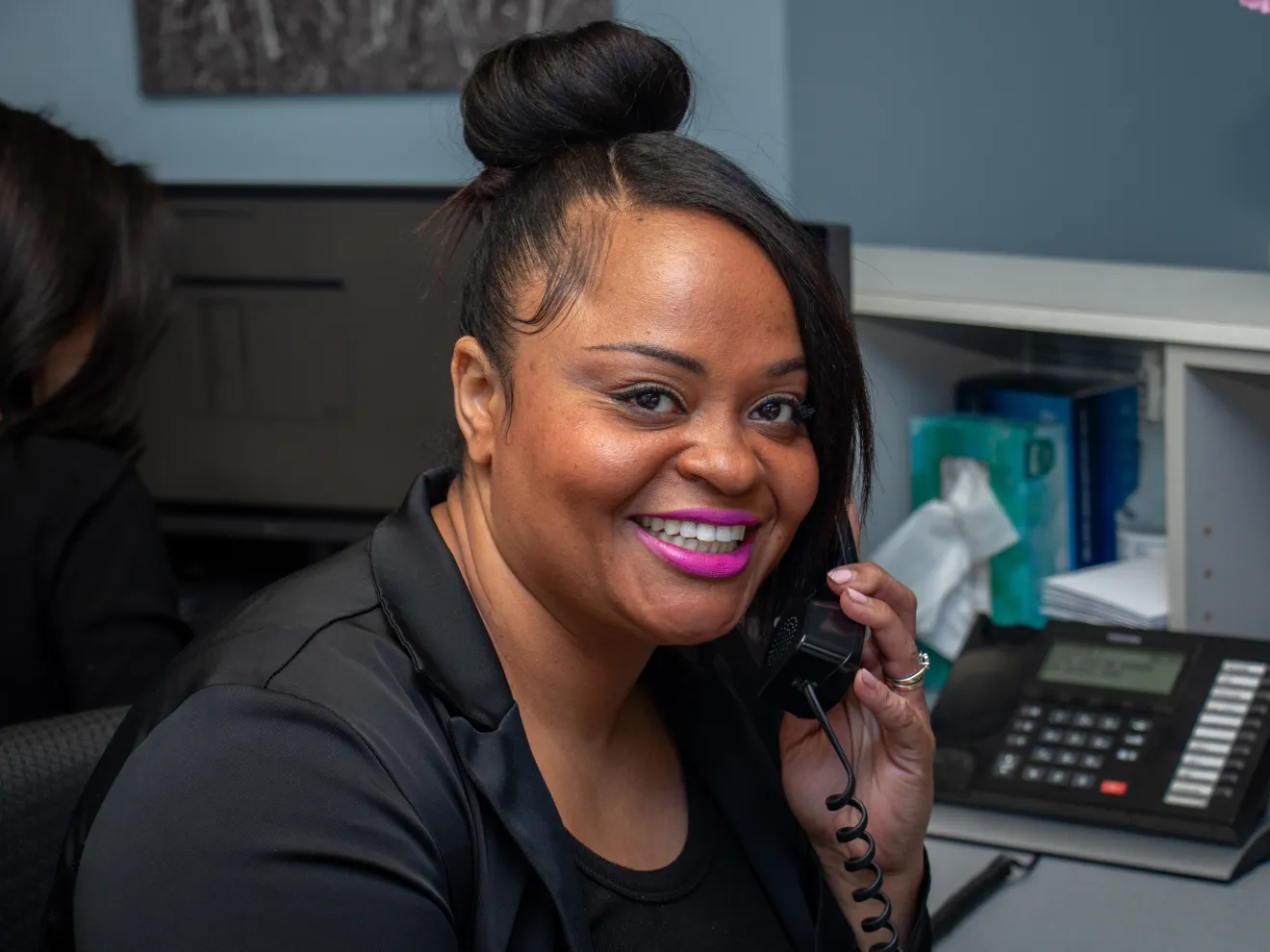 A woman in an office smiles while talking on the phone.