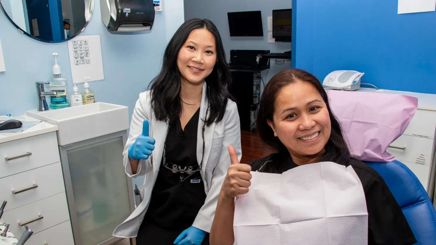A dentist and a patient both give thumbs up in a dental clinic.