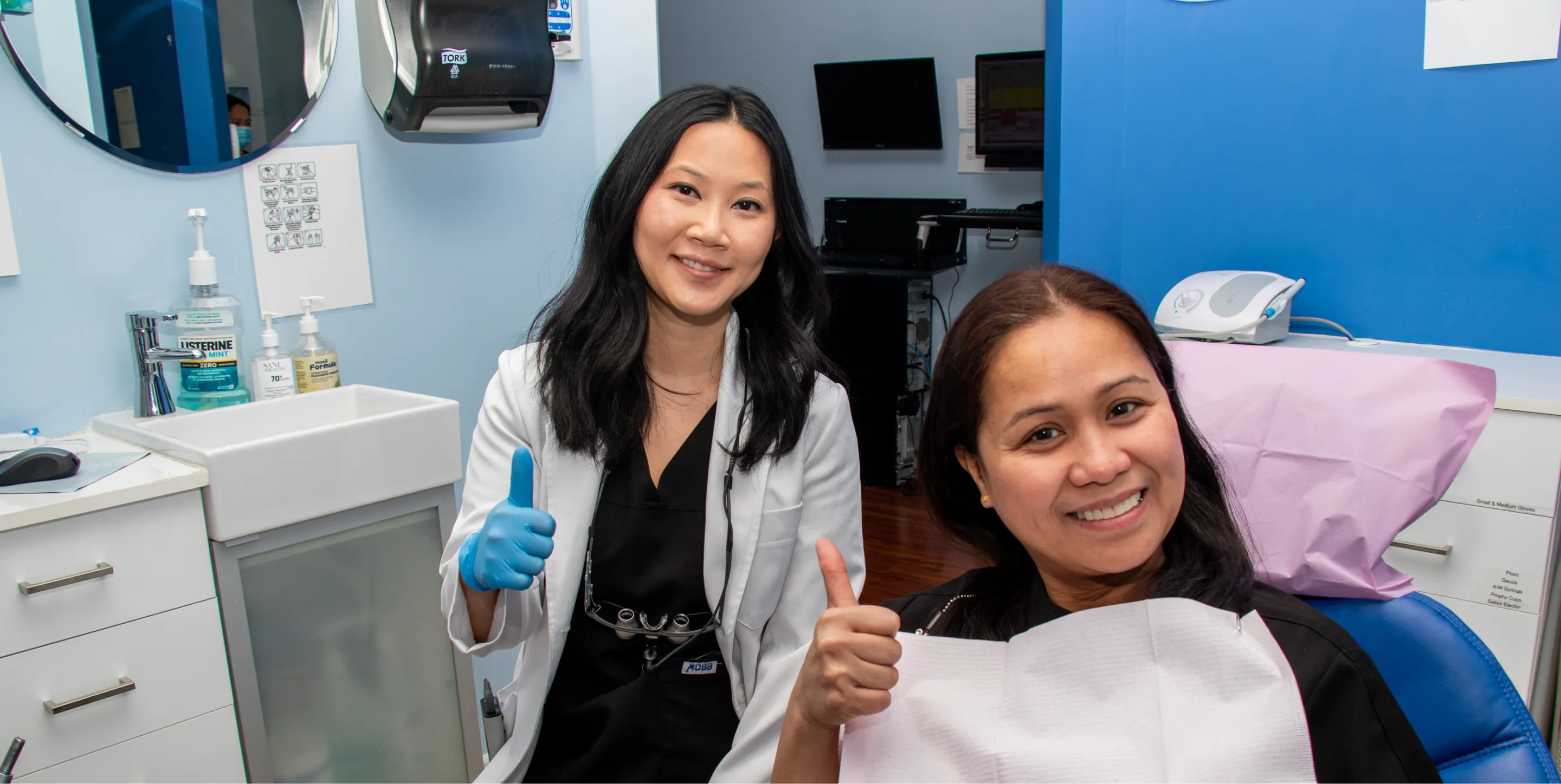 A dentist and patient both give a thumbs up in a dental clinic.