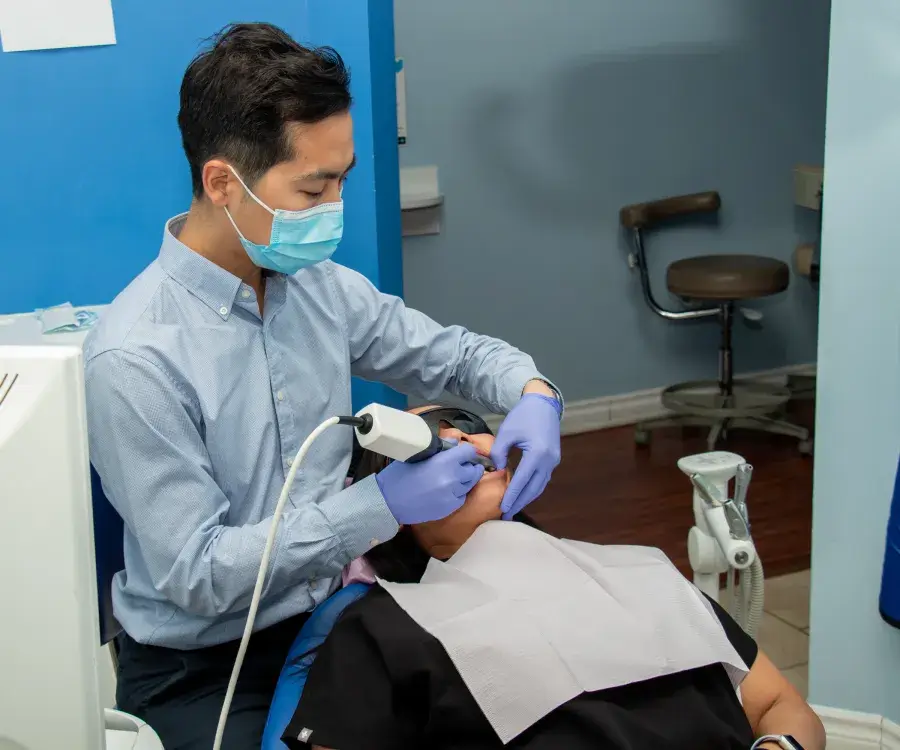 Dentist wearing gloves and mask examines a patient's teeth using a dental tool.