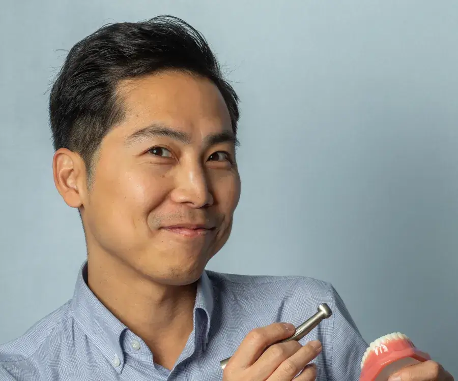A person holding a dental model and a dental tool, smiling at the camera.
