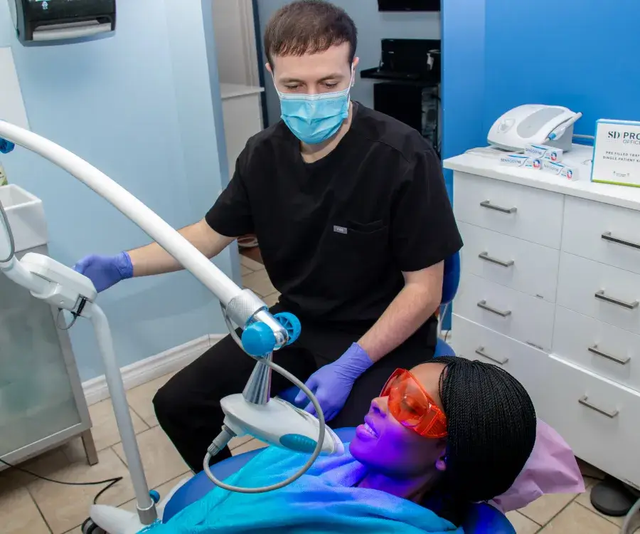 A dental professional performs a teeth whitening procedure on a patient wearing protective glasses.