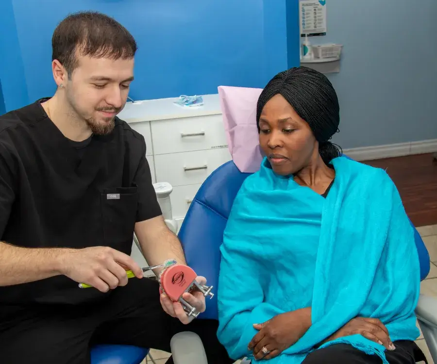 A dentist explains a dental model to a woman sitting in a dental chair.