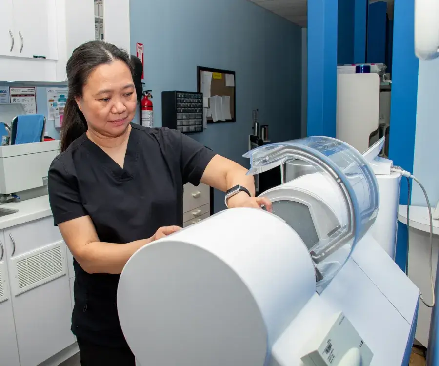 A woman in scrubs operates a medical machine in a clinic setting.