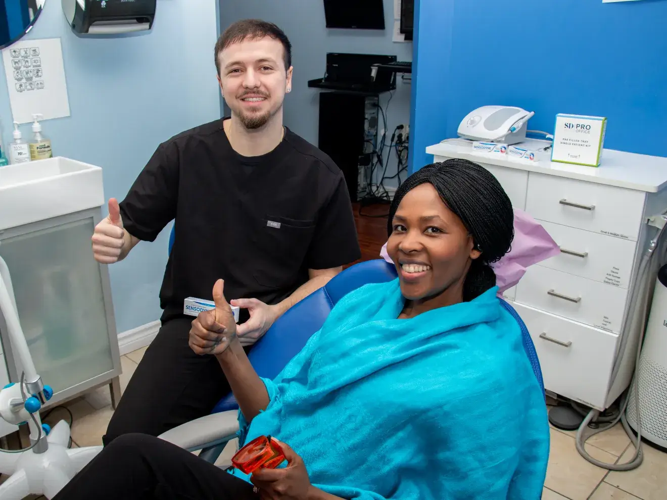 A dentist and a patient both give a thumbs up in a dental office.
