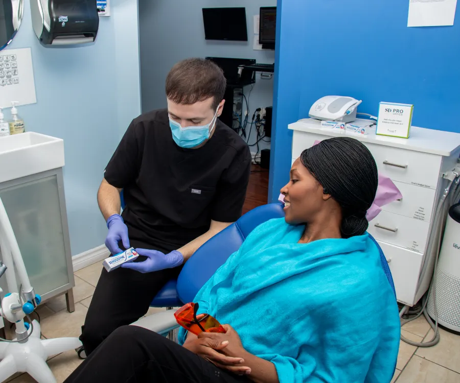 A dental professional explains a product to a patient sitting in a dental chair.