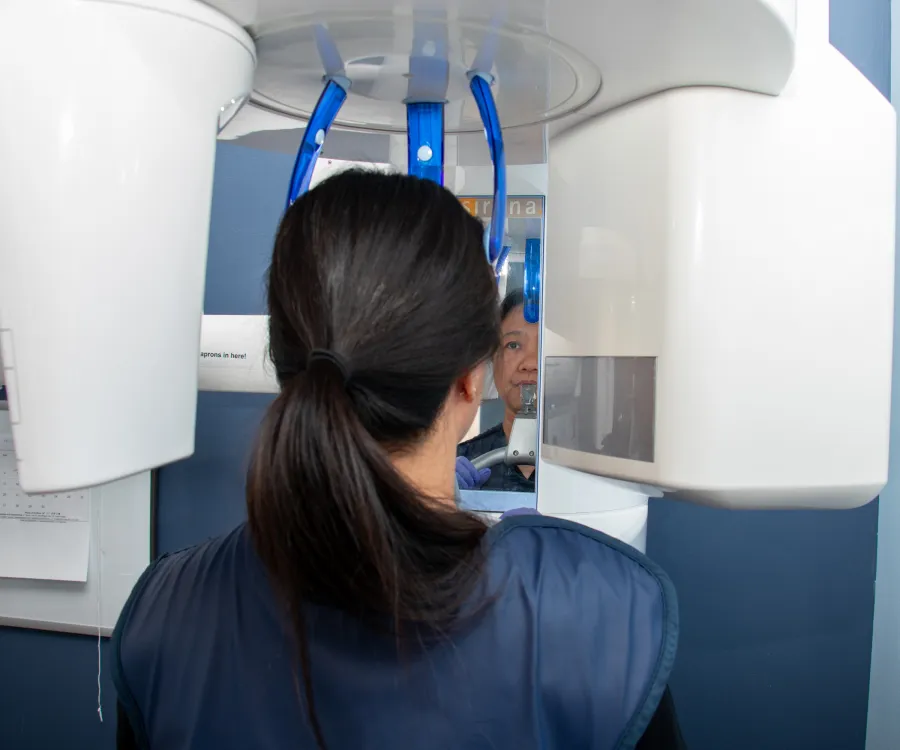 A person undergoes a dental X-ray, sitting in front of a large white machine.