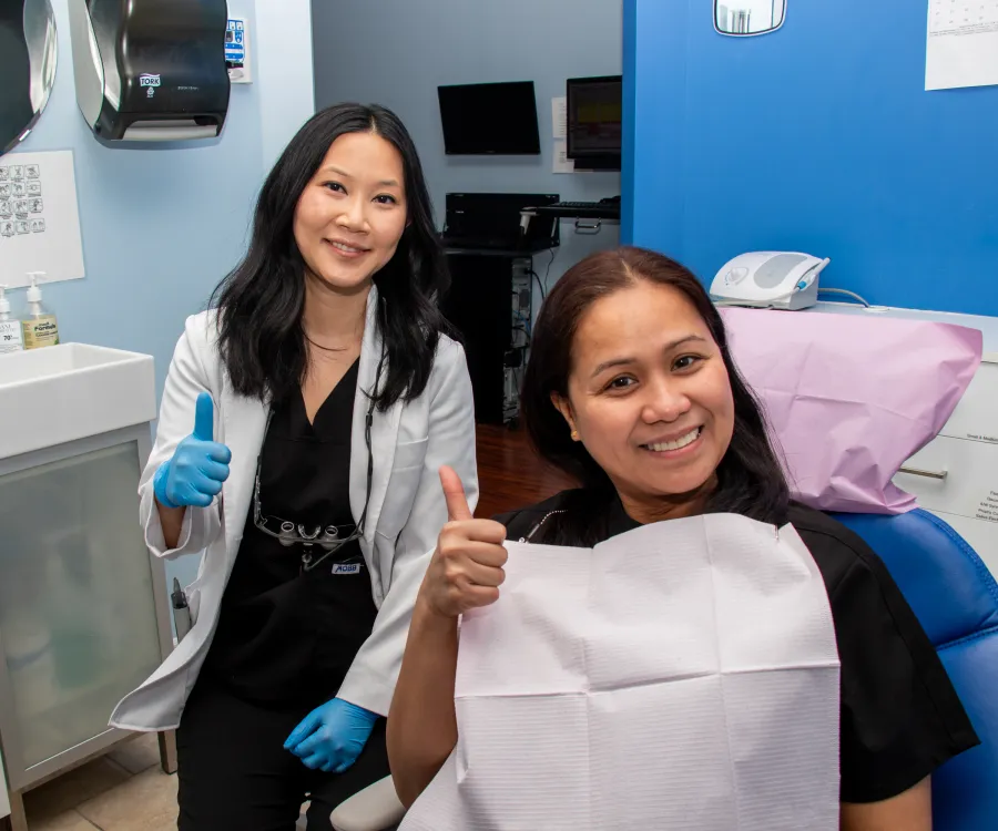 A dentist and a patient smile and give thumbs up in a dental office.