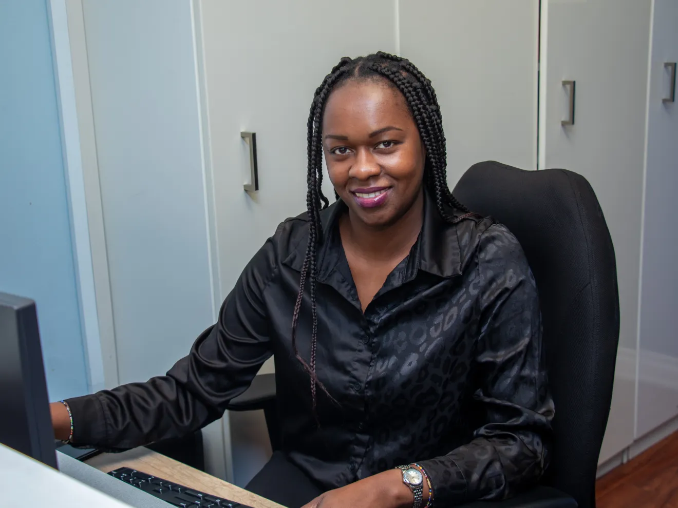 A woman sitting at a desk is smiling while using a computer.