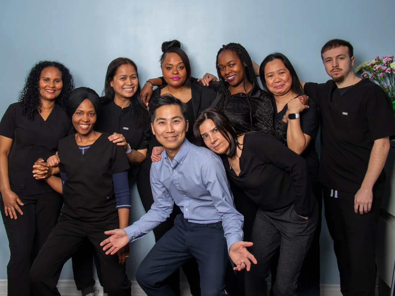 A group of nine people poses together, smiling, in front of a blue wall.