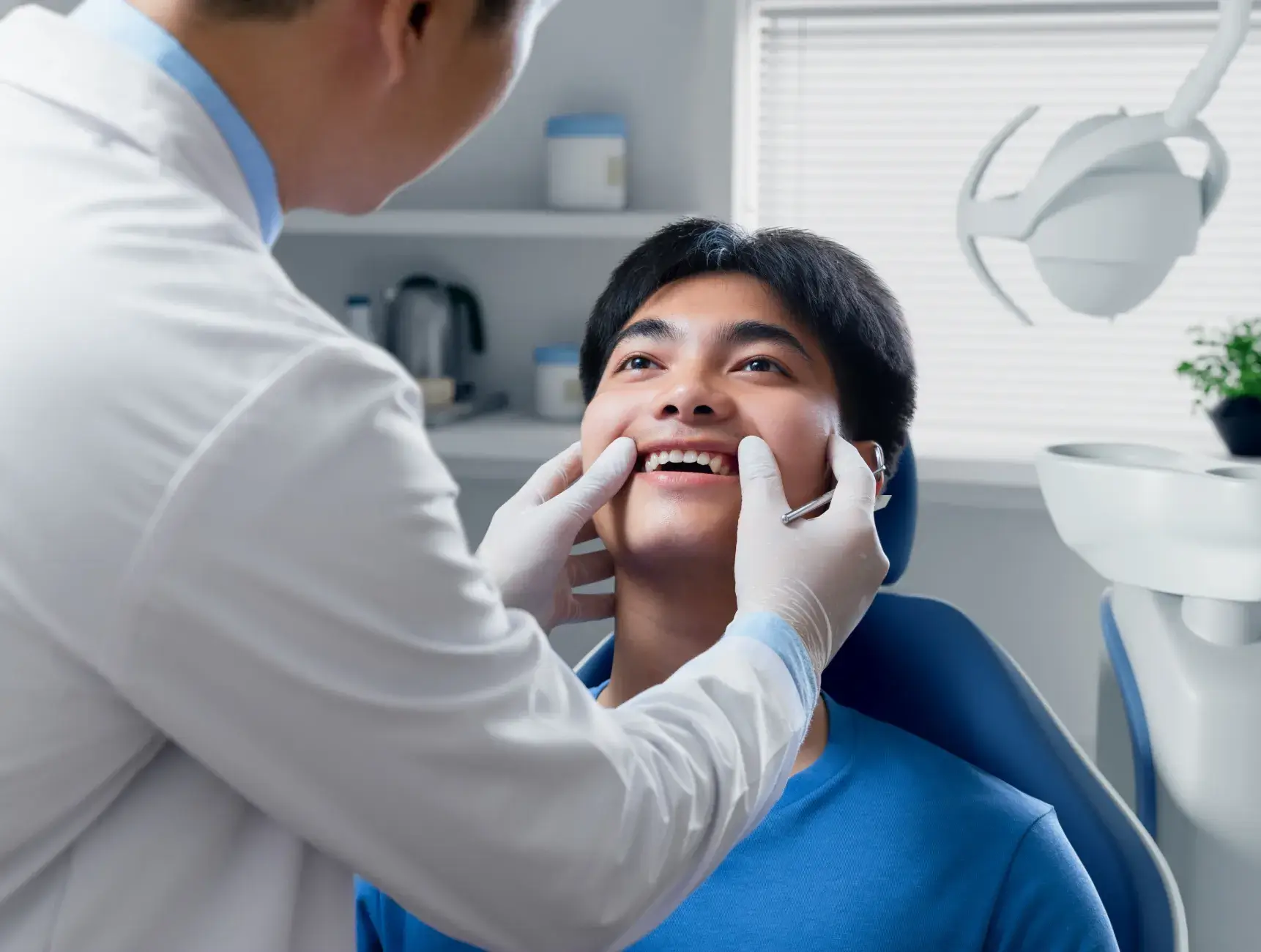 A dentist examines a smiling patient's teeth in a dental office.