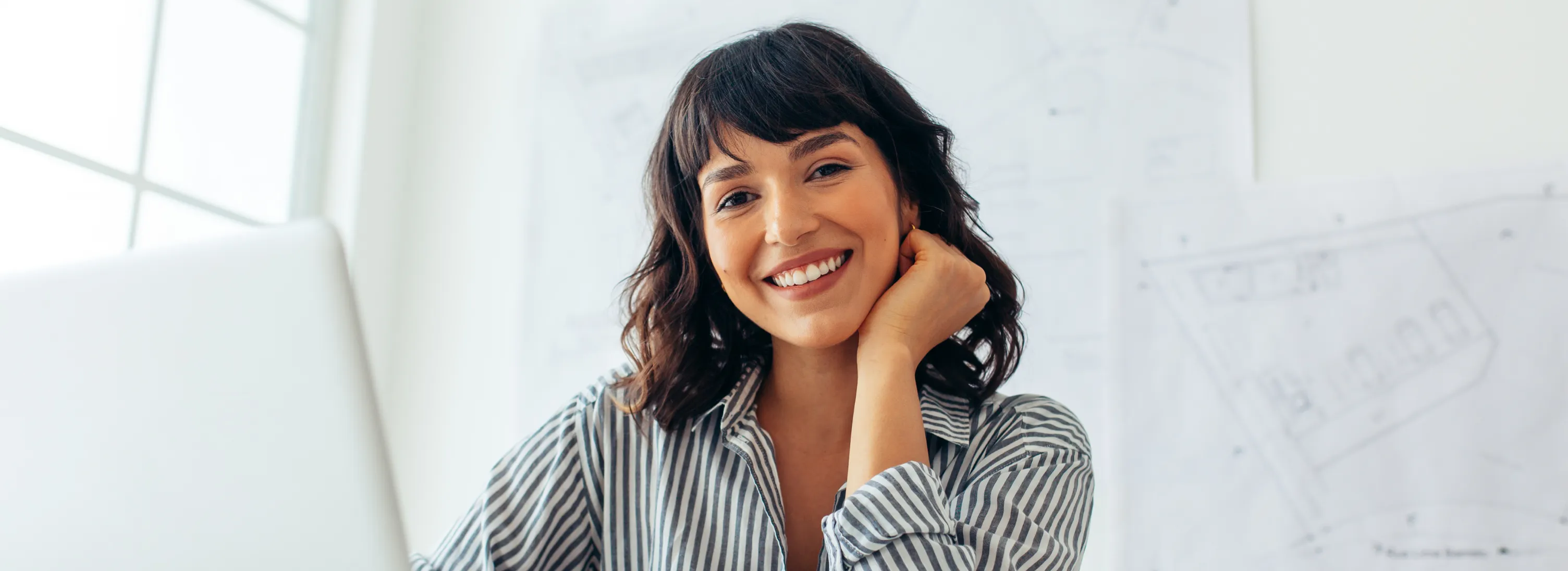 A person in a striped shirt sits at a desk, smiling directly at the camera.