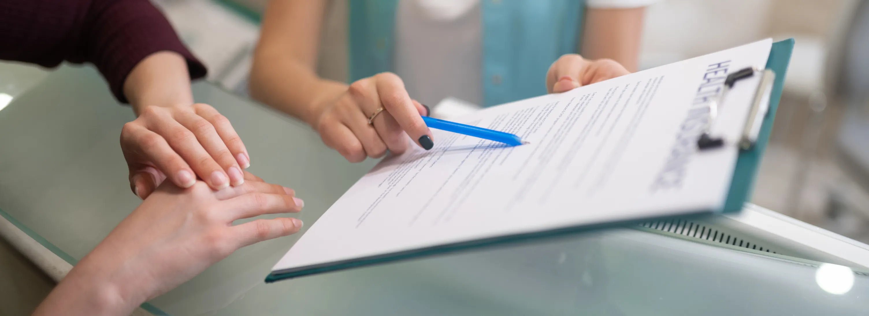 Hands pointing at a clipboard while one person holds a pen over a document.