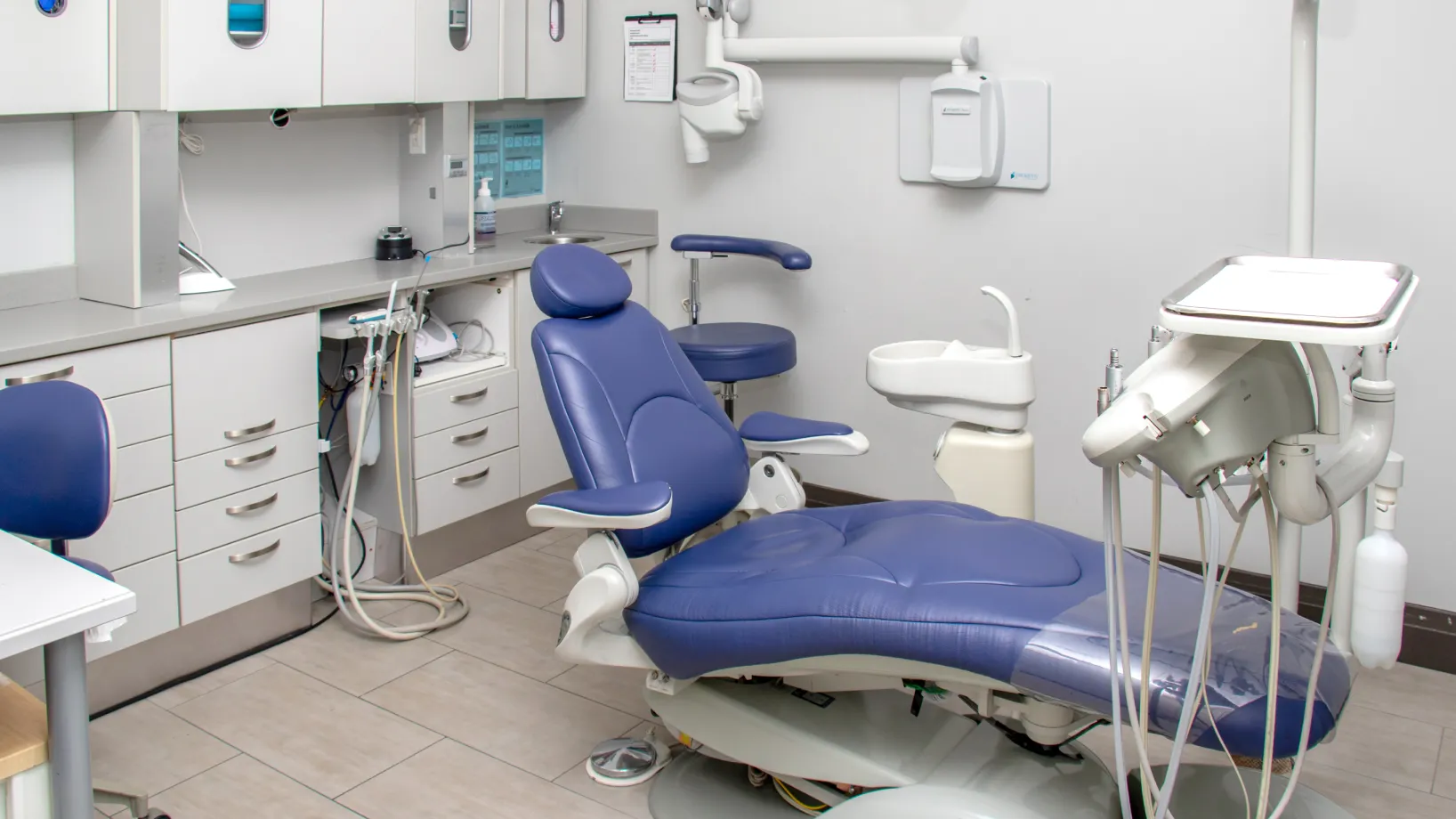 A dental office with a blue dentist chair, equipment, and white cabinets.