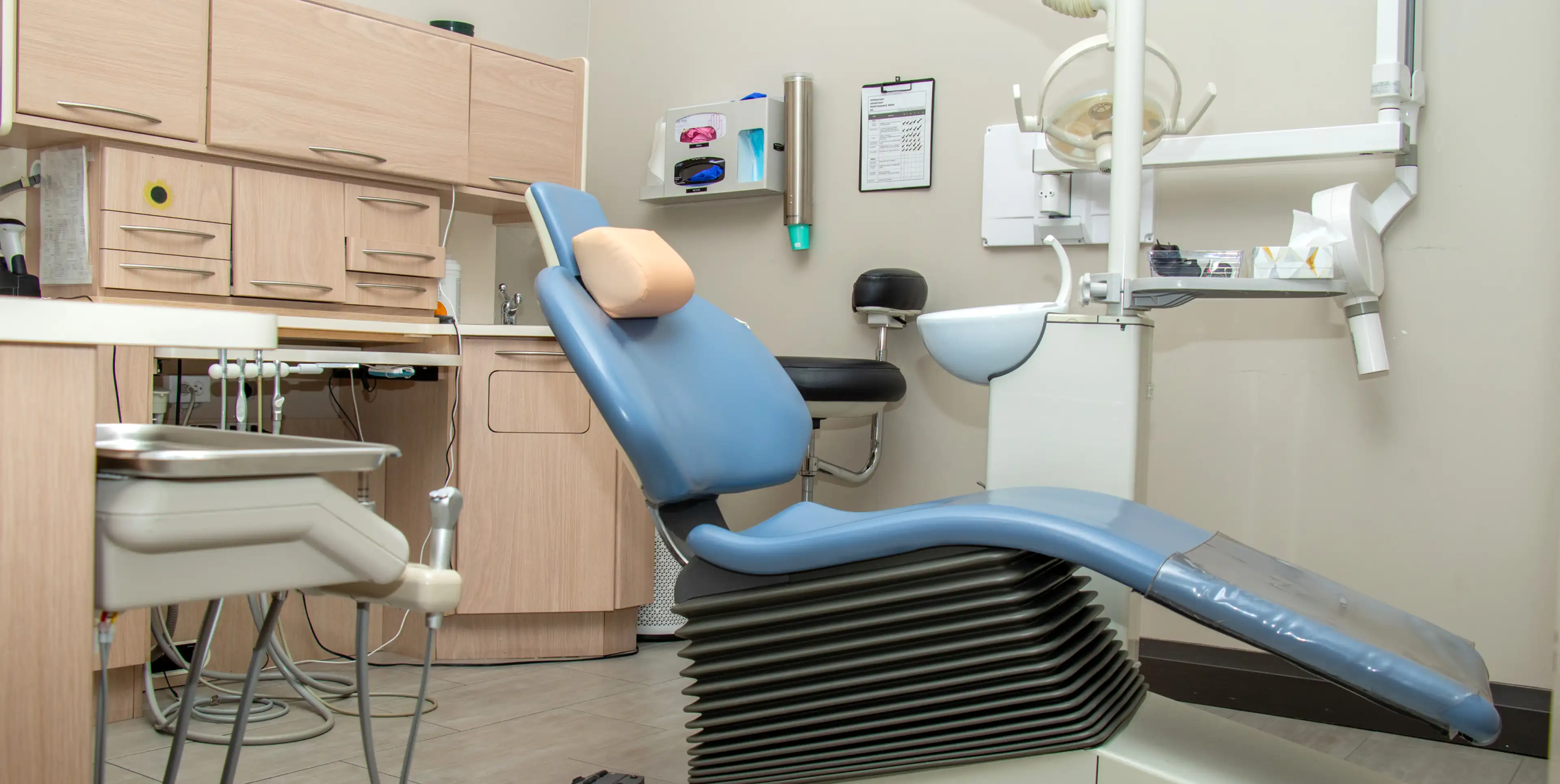 A dentist's chair in an empty dental office with cabinets and dental equipment nearby.