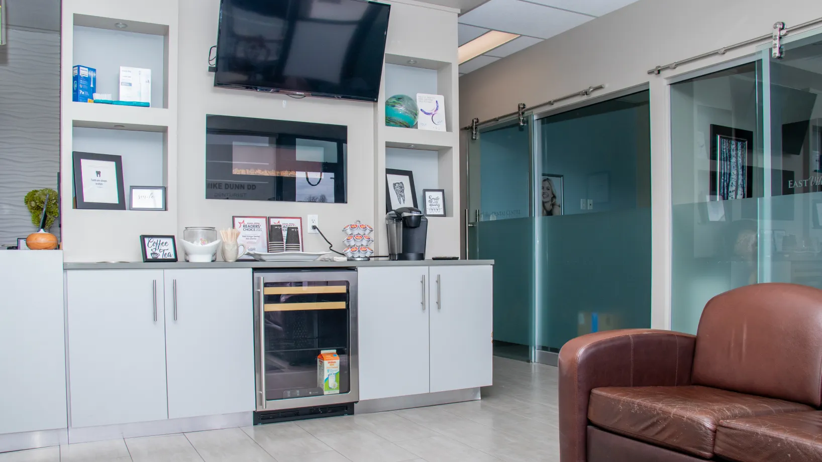 A modern waiting room with a white cabinet, a TV, and a brown leather chair.