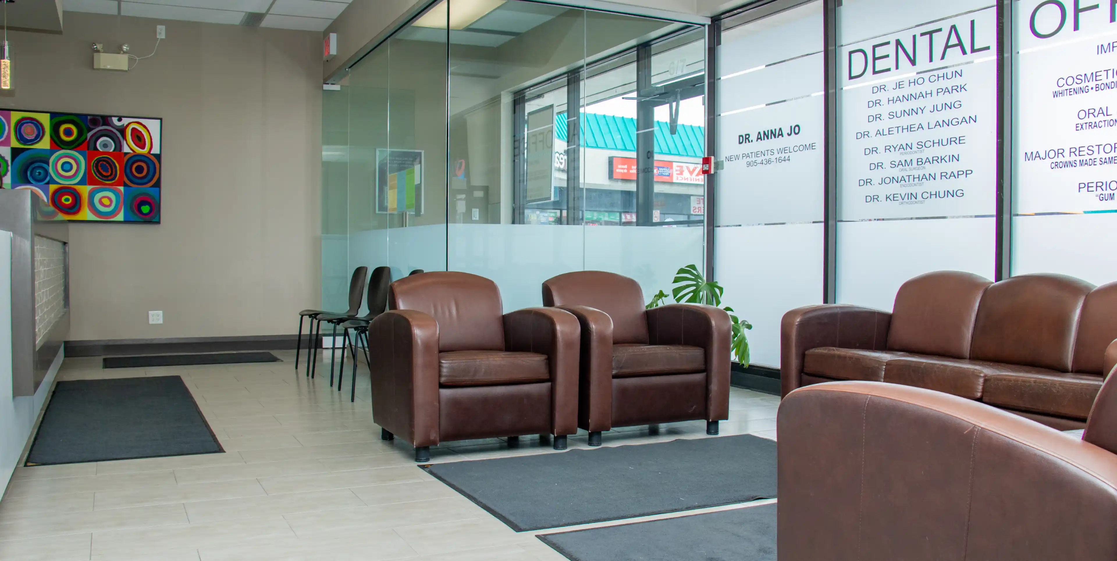 A waiting room with brown leather chairs and a glass wall featuring dentist names.