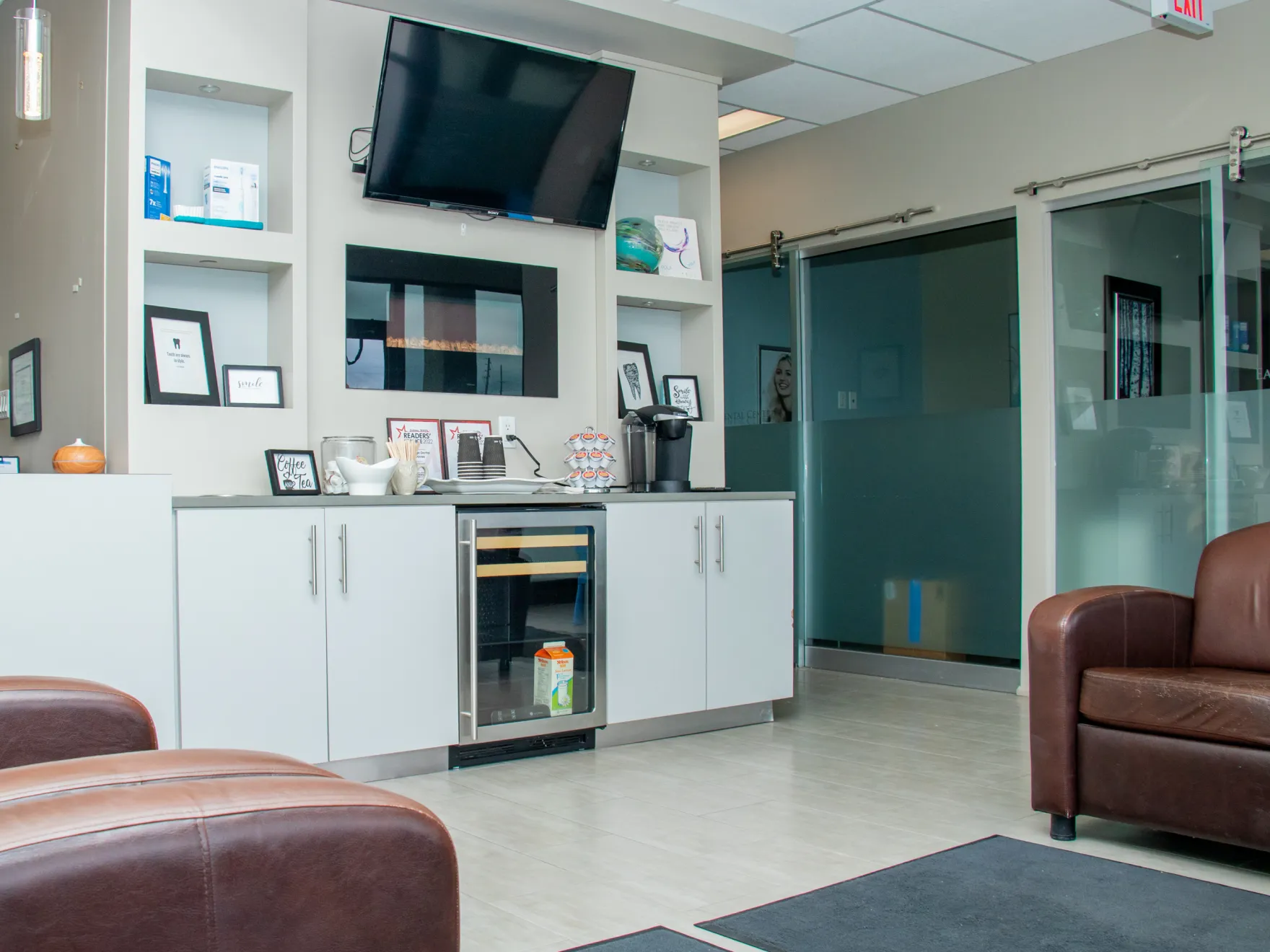A waiting room with brown chairs, a television on the wall, and a cabinet below.