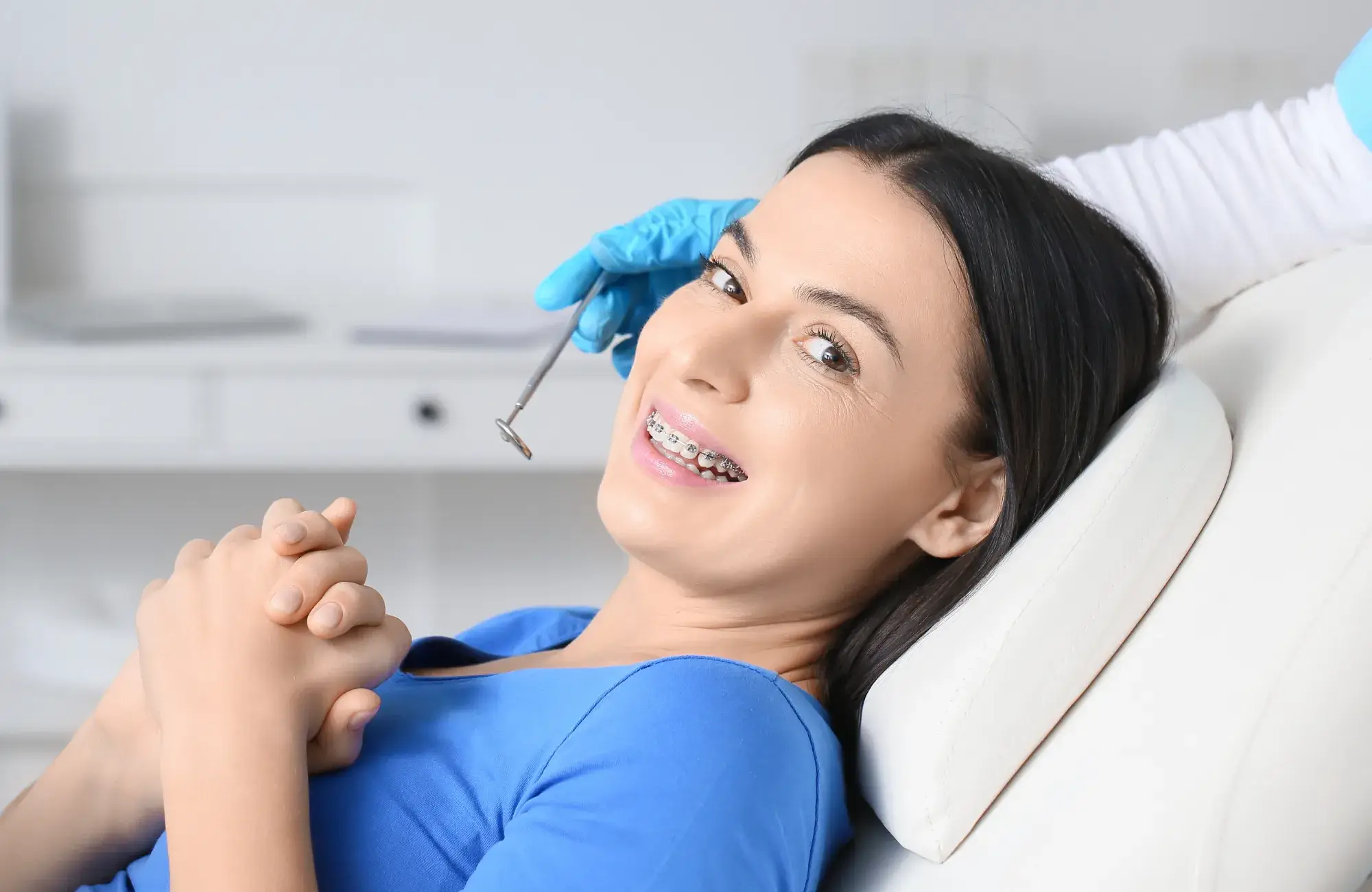 A woman with braces smiles while sitting in a dental chair.