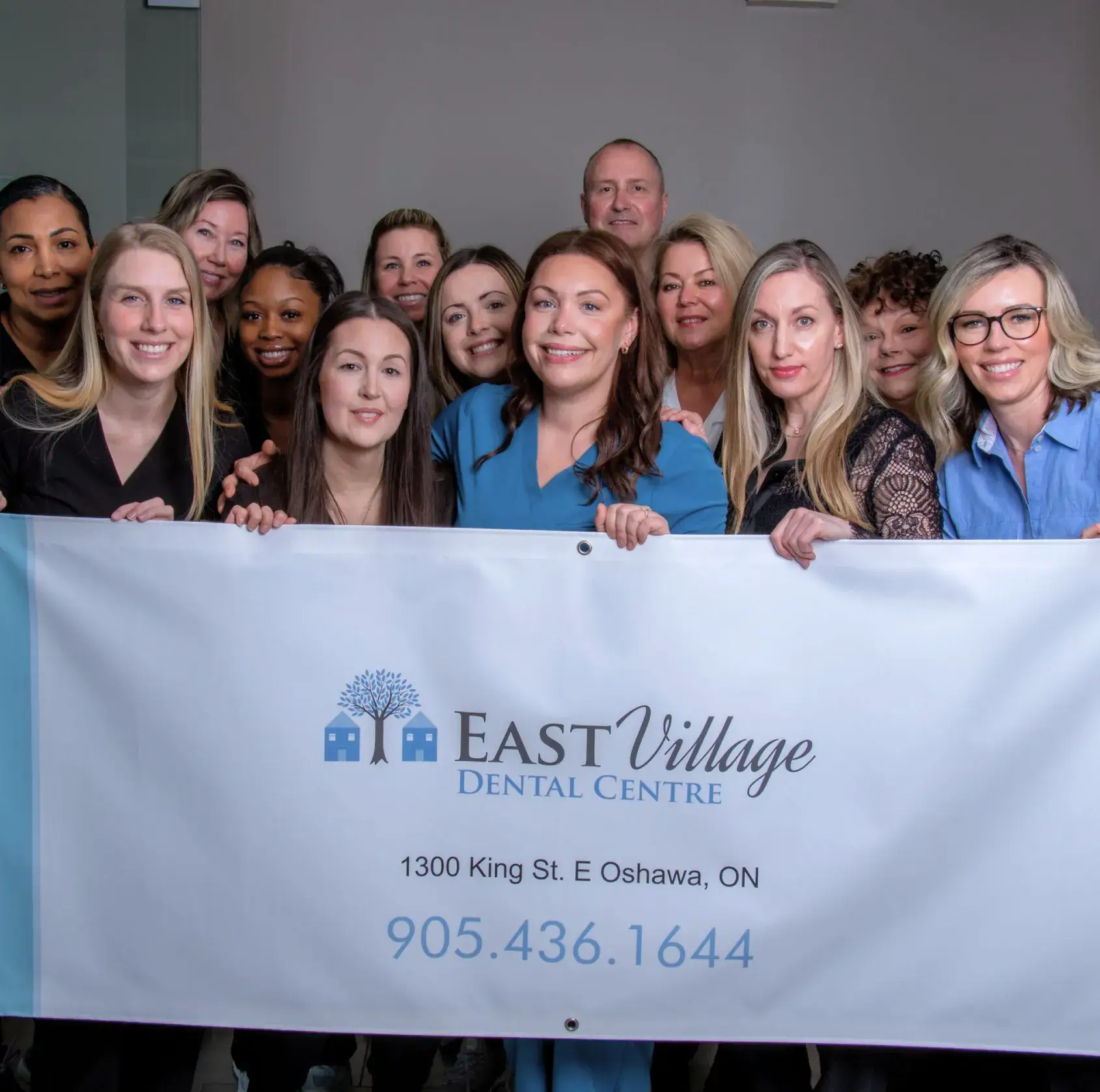 Group of people smiling and holding a banner for East Village Dental Centre with contact information.