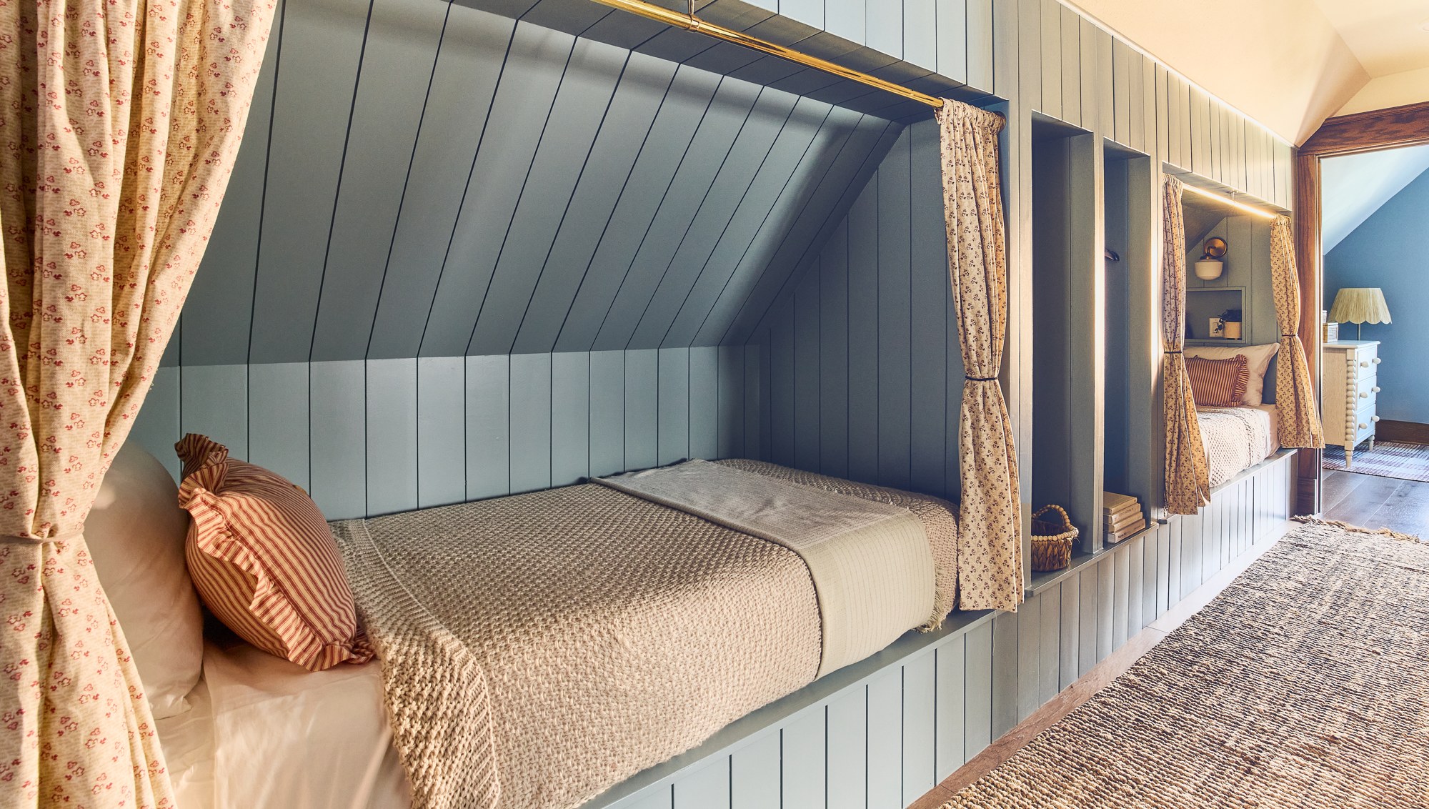 Finished sleeping alcoves with blue paneling and patterned curtains beneath the sloping roof.